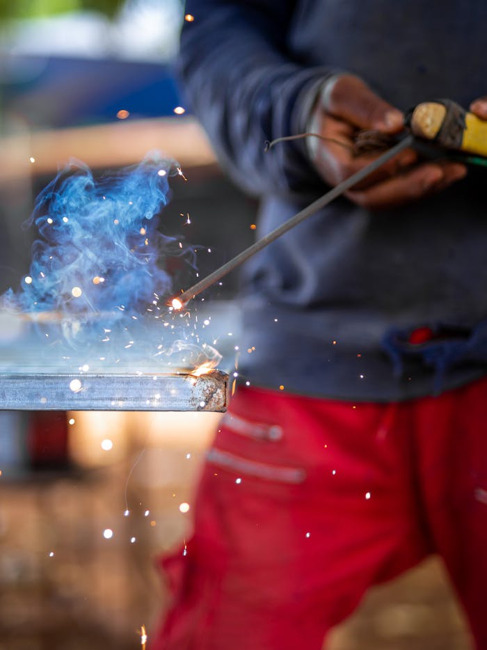 Close-up of a welder working on metal with visible sparks and smoke for industrial use.